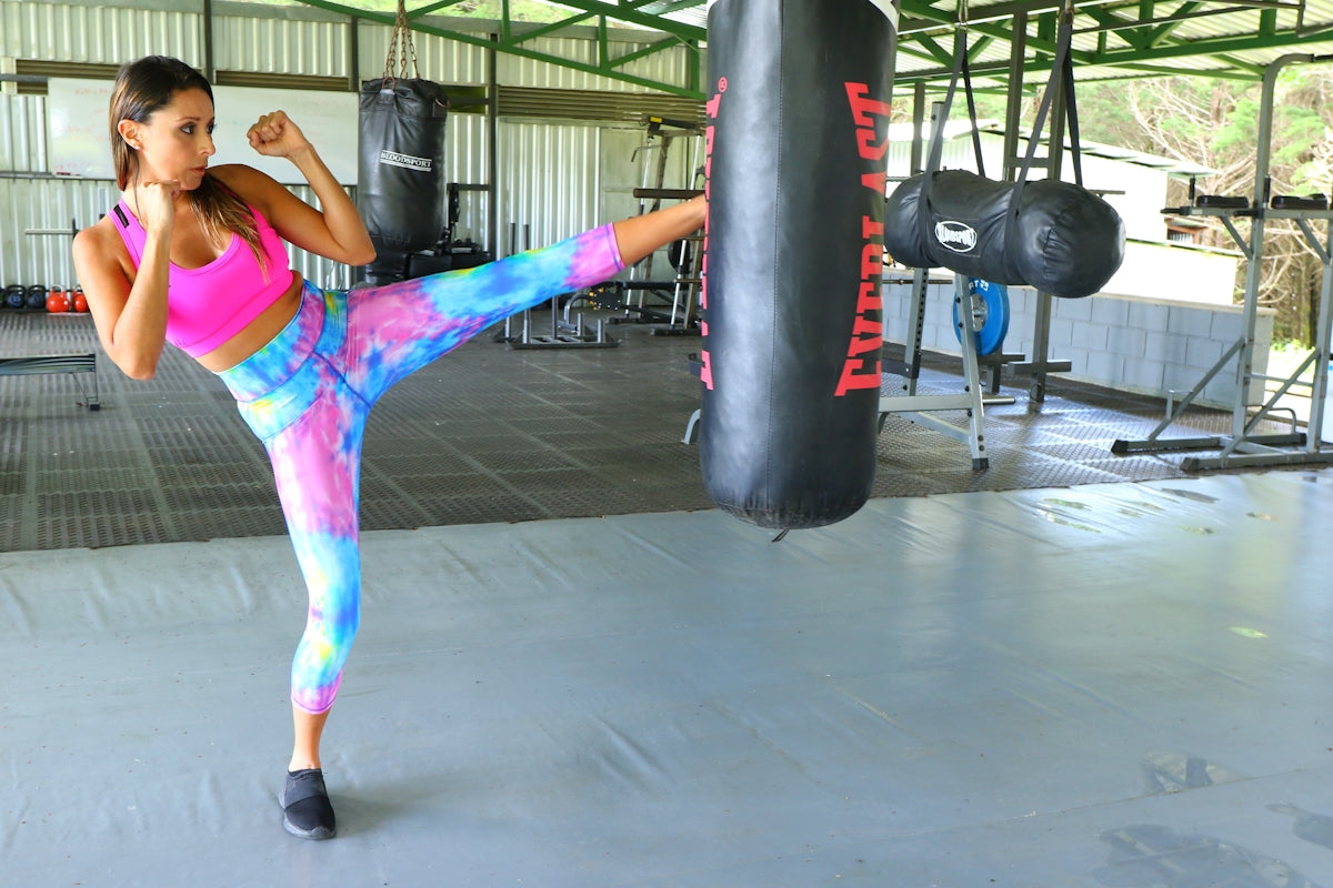woman in pink tank top and purple shorts standing beside black heavy bag