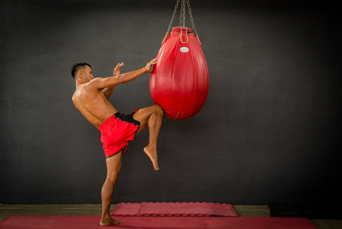 A man in red shorts kicking a red boxing bag