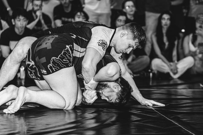 Two men grappling on a mat with spectators watching